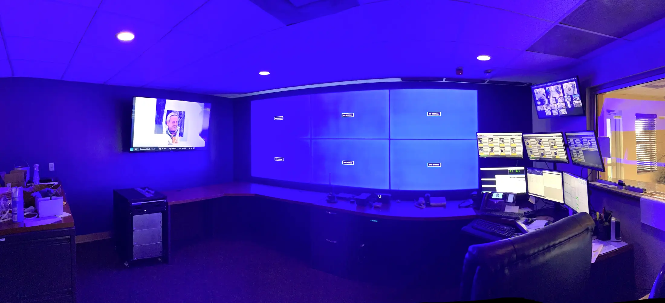 A control room with a four panel video wall, a curved operator console, a bank of monitors and blue accent lighting.
