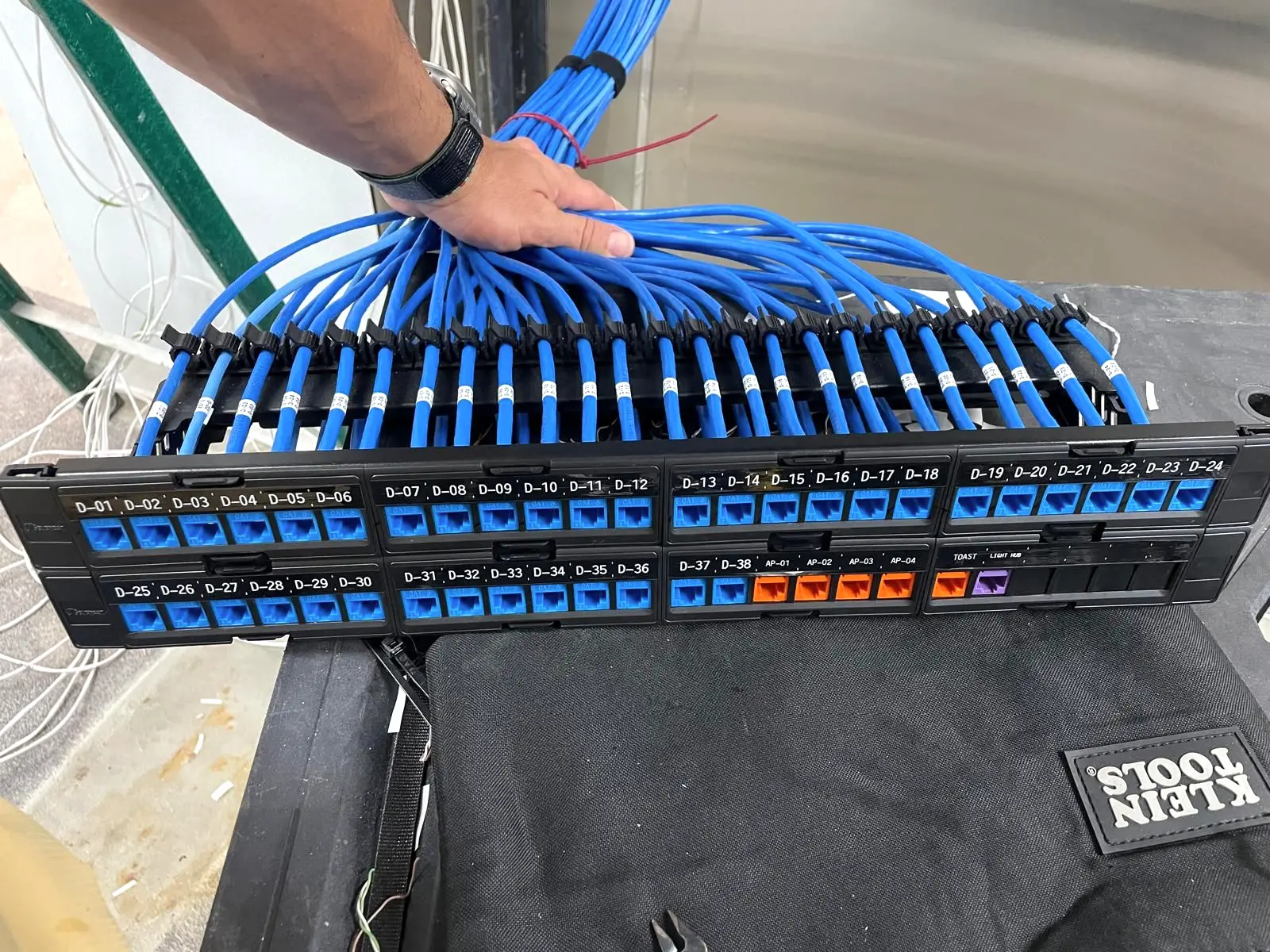 A twenty four port keystone patch panel being terminated on a tool bag, with labelled blue jacks for data and orange jacks for wireless access points.