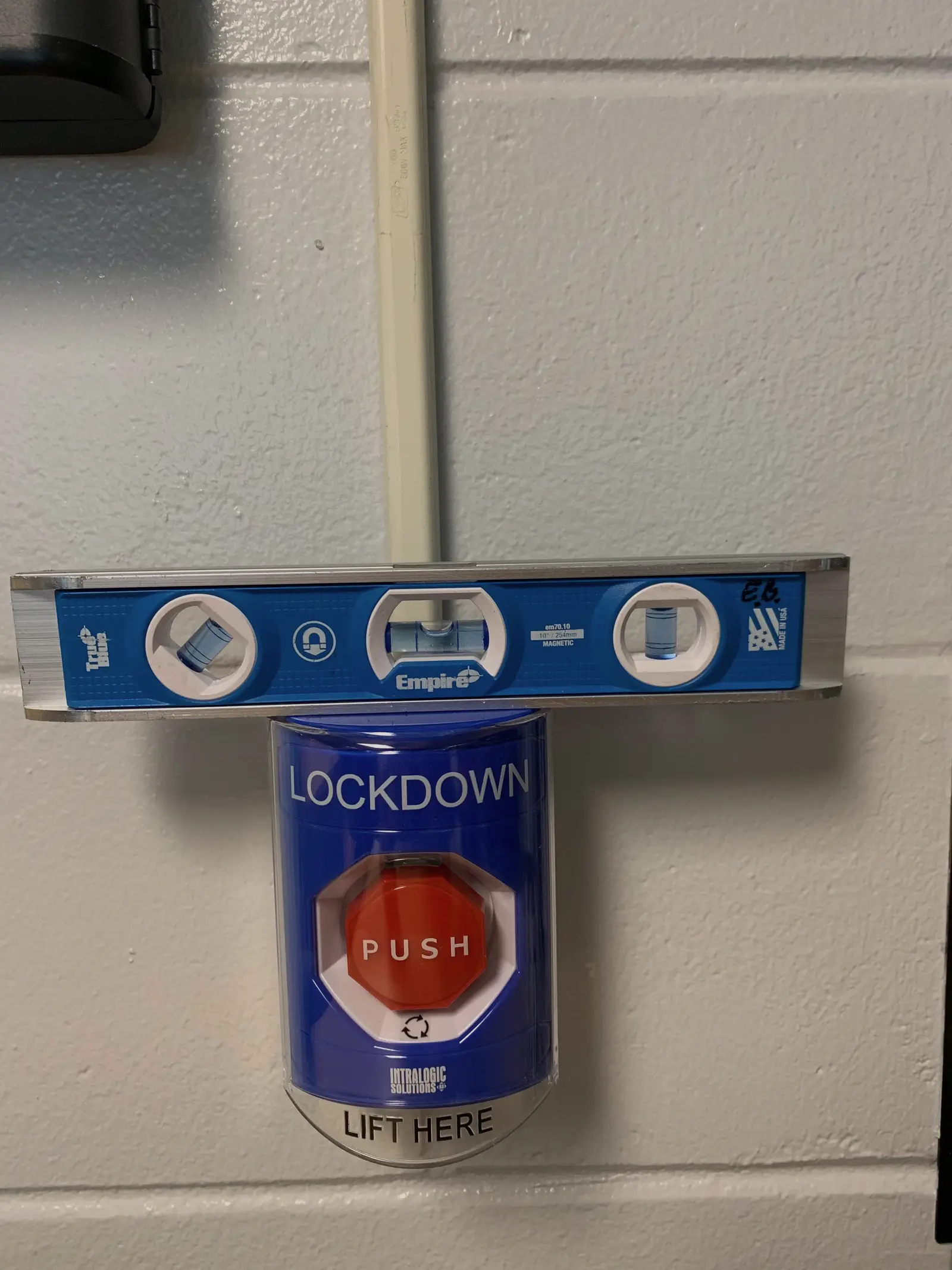 A magnetic spirit level held across a covered lockdown call point to check it sits square before final fixing.