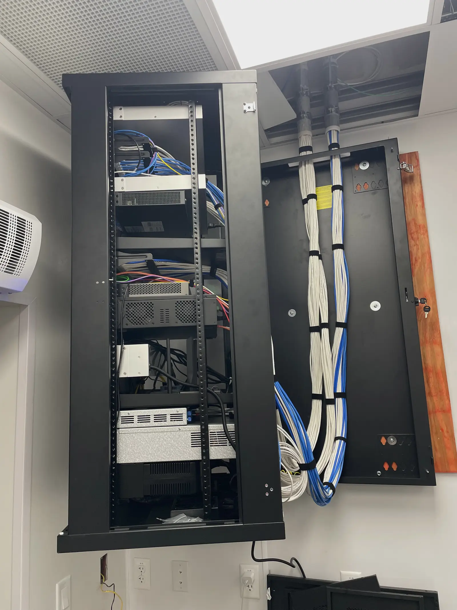 A wall mounted swing out rack standing open, the cable bundles on its hinged back panel combed straight and strapped at even intervals where they come down from the conduit.